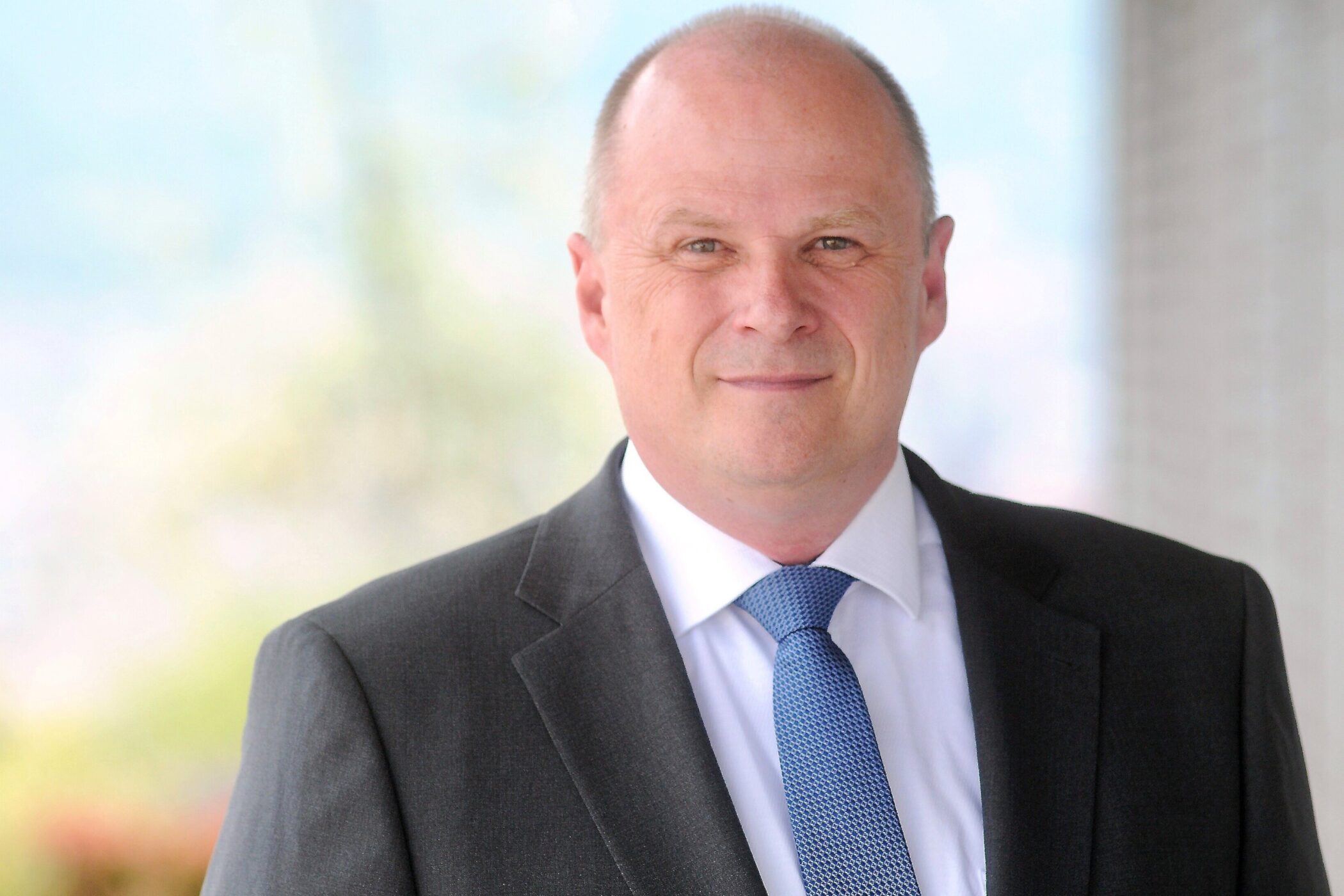 Glatzenmann in Anzug mit blauer Krawatte.