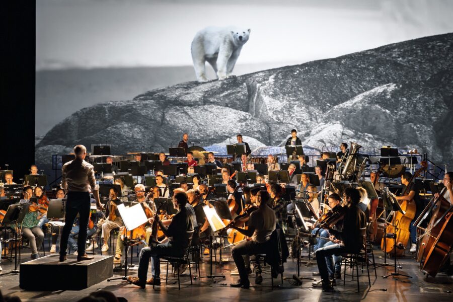Dirigent und Orchester vor Großbild mit Eisbär.
