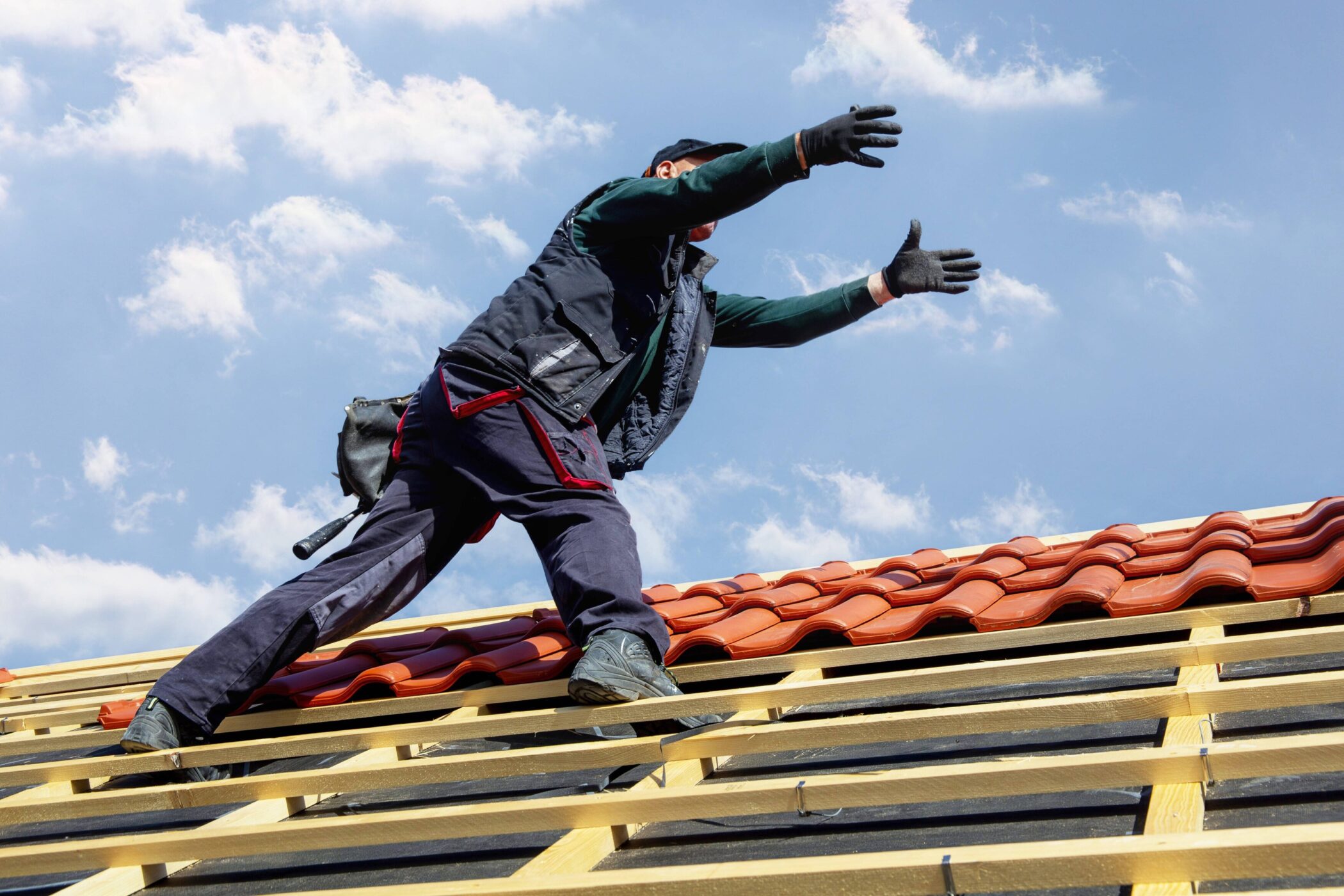 Person auf einem Dach, trägt Handschuhe, hat die Arme ausgestreckt.