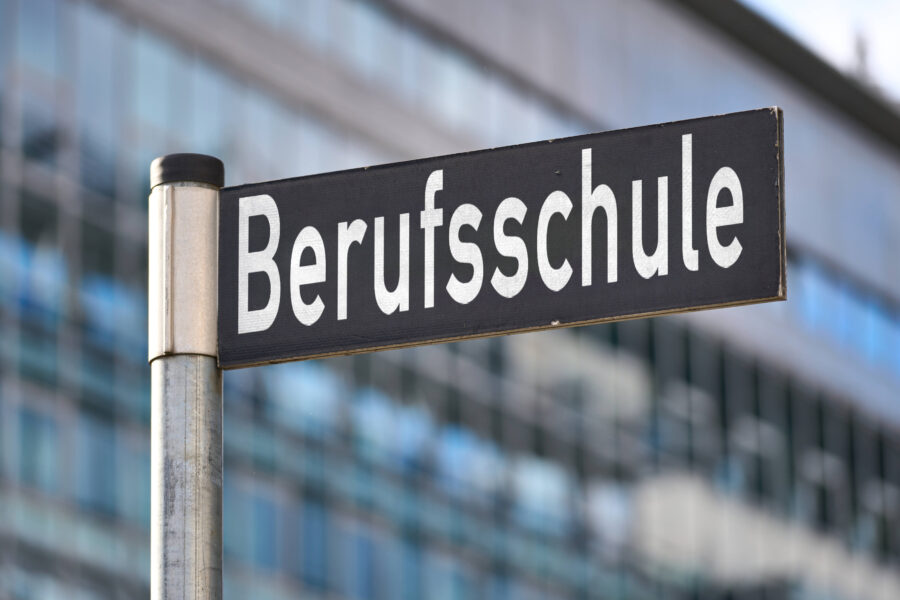 Schild mit der Aufschrift "Berufsschule" vor unscharfem Gebäude.