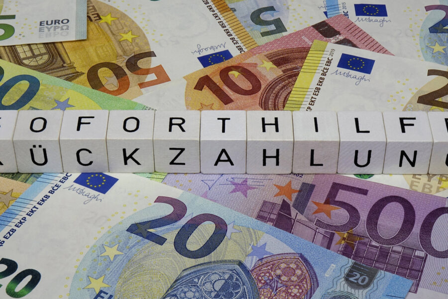 Buchstabenwürfel „SOFORTHILFE RÜCKZAHLUNG“ auf Euro-Geldscheinen.