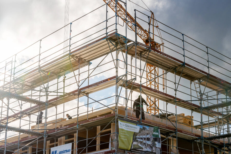 Gerüst mit Bauarbeitern, Baukran im Hintergrund, teilweise bewölkter Himmel.