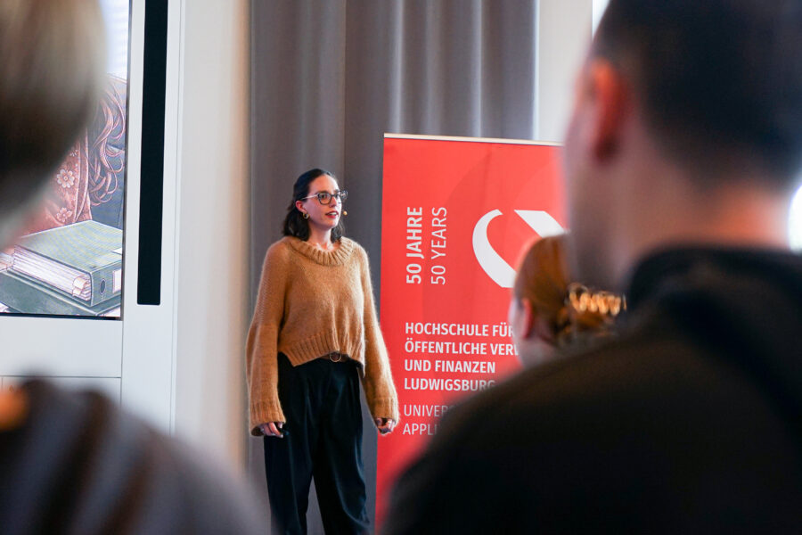 Eine Person spricht vor einem roten Banner mit Aufschrift „50 Jahre Hochschule“.