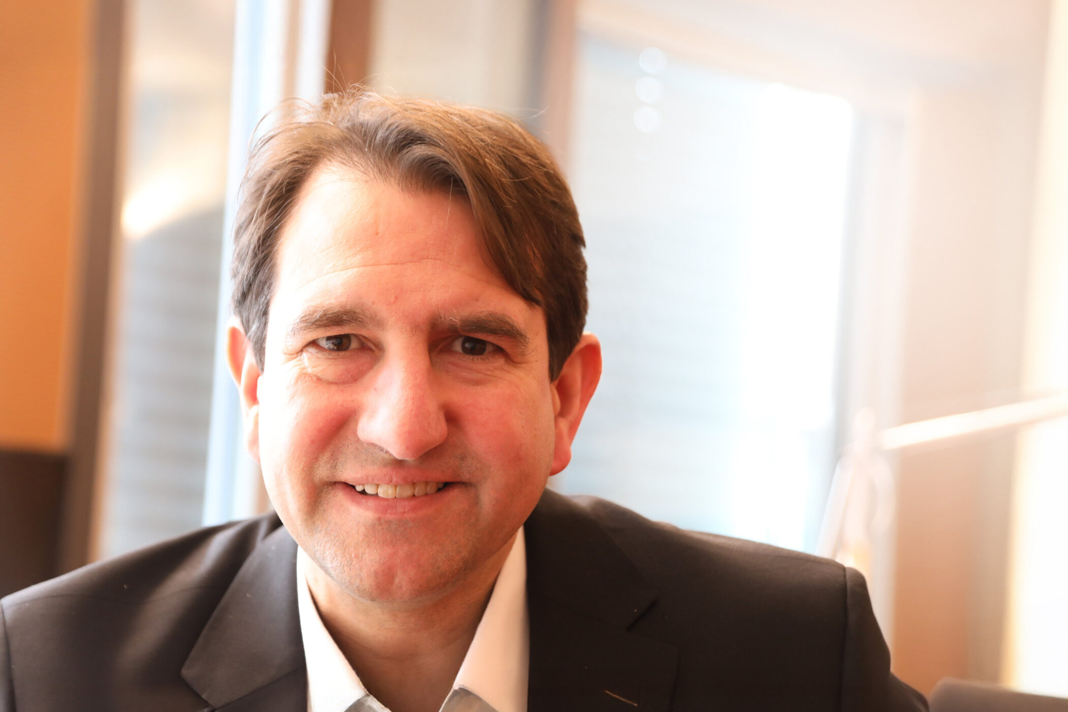 Mann in Anzug lächelt in die Kamera, im Hintergrund Fenster.