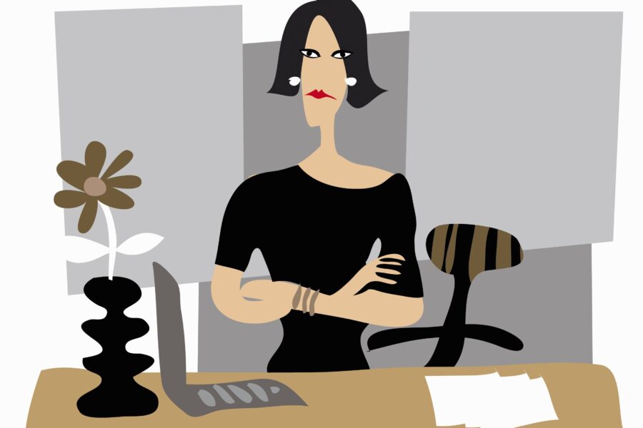 Frau in Schwarz sitzt am Schreibtisch mit Vase, Blume und Laptop.