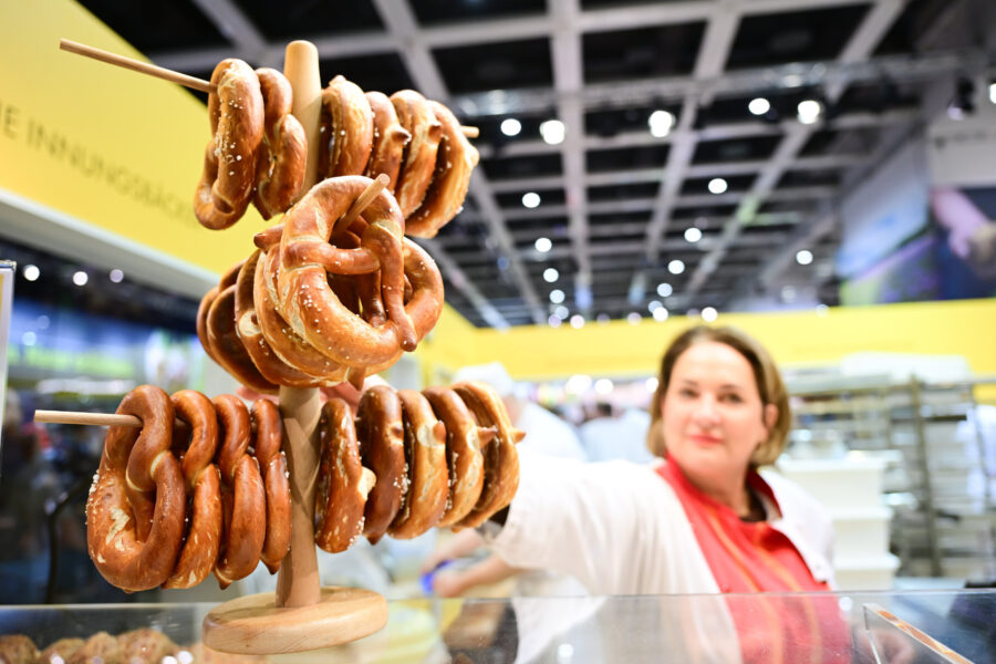 Mehrere Brezeln auf Holzständer, unscharfe Person greift nach einer Brezel.