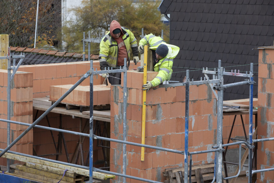 Zwei Bauarbeiter mauern auf einer Baustelle mit rotem Ziegelstein.