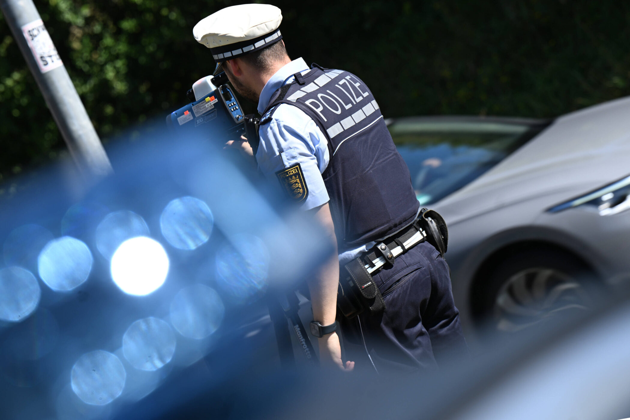Polizist in Uniform mit Radarpistole, blauer Lichtreflex im Vordergrund.