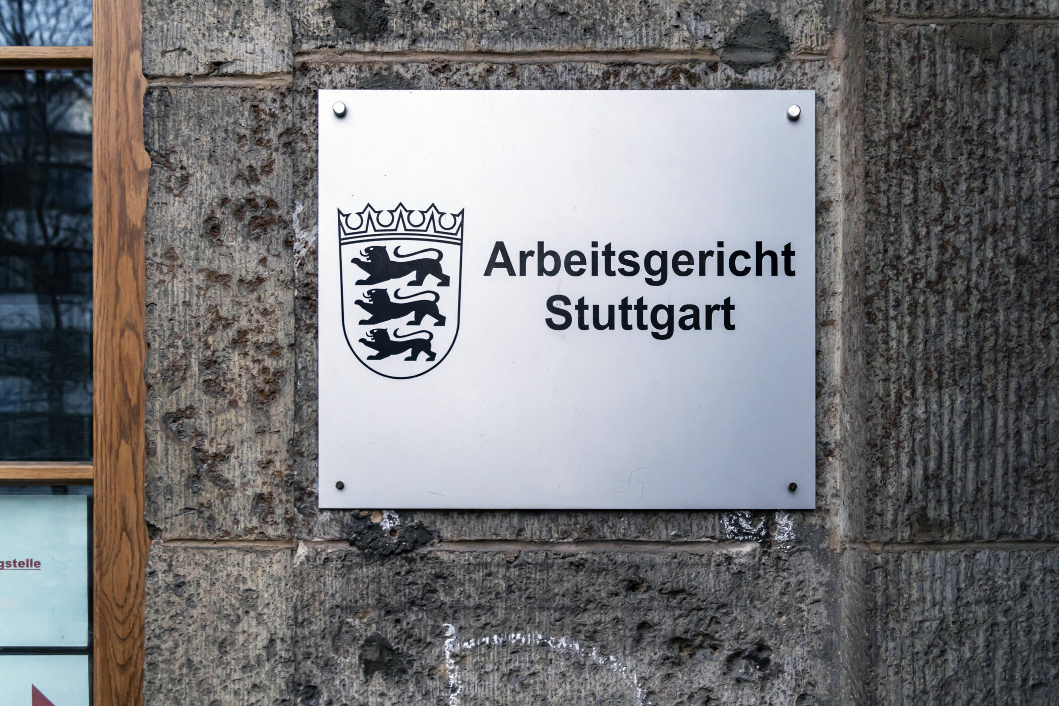 Schild mit Aufschrift "Arbeitsgericht Stuttgart" an einer Steinwand.