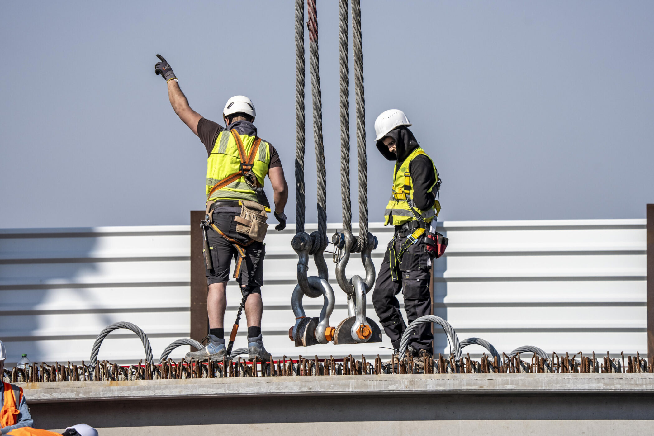 Zwei Arbeiter mit Helmen und Warnwesten stehen auf einer Baustelle.