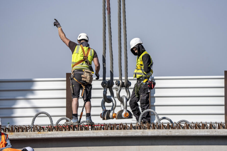 Zwei Arbeiter mit Helmen und Warnwesten stehen auf einer Baustelle.