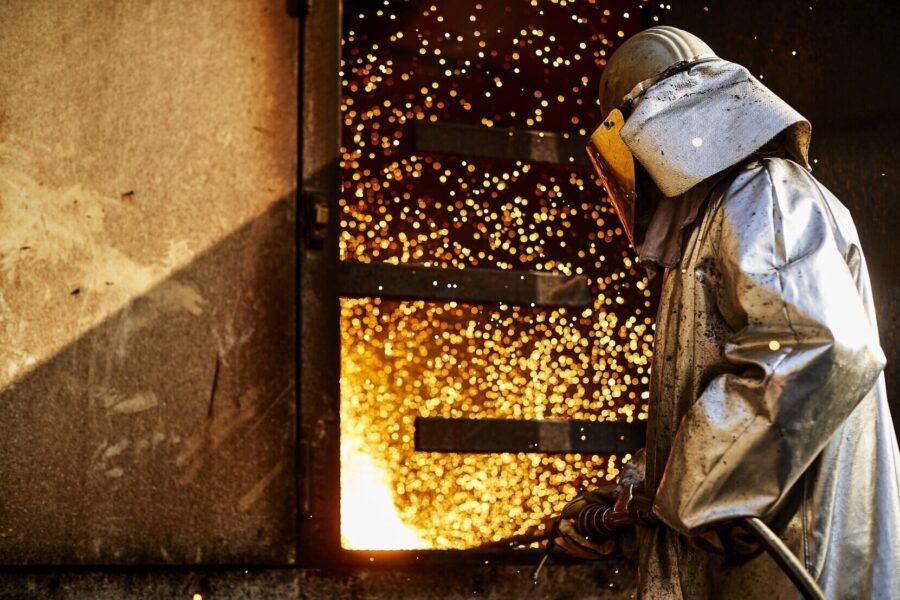Person in Schutzkleidung vor Funken sprühendem Ofen.