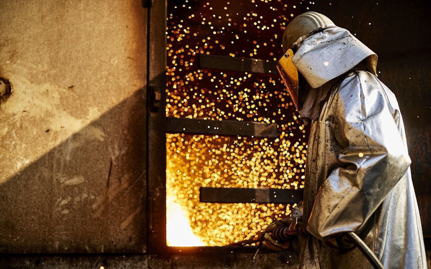 Person in Schutzkleidung vor Funken sprühendem Ofen.