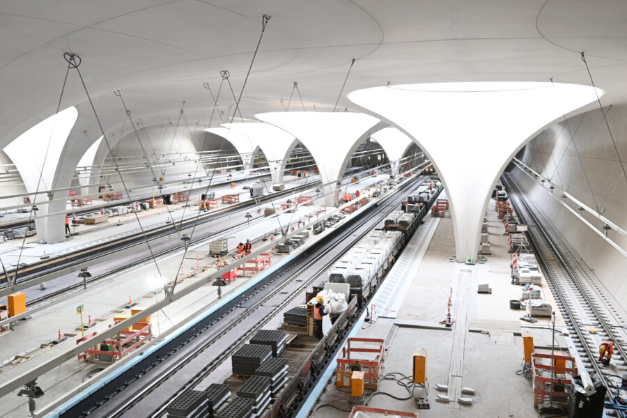 Großer unterirdischer Bahnhof im Bau mit mehreren Gleisen und Arbeitern in Warnwesten.