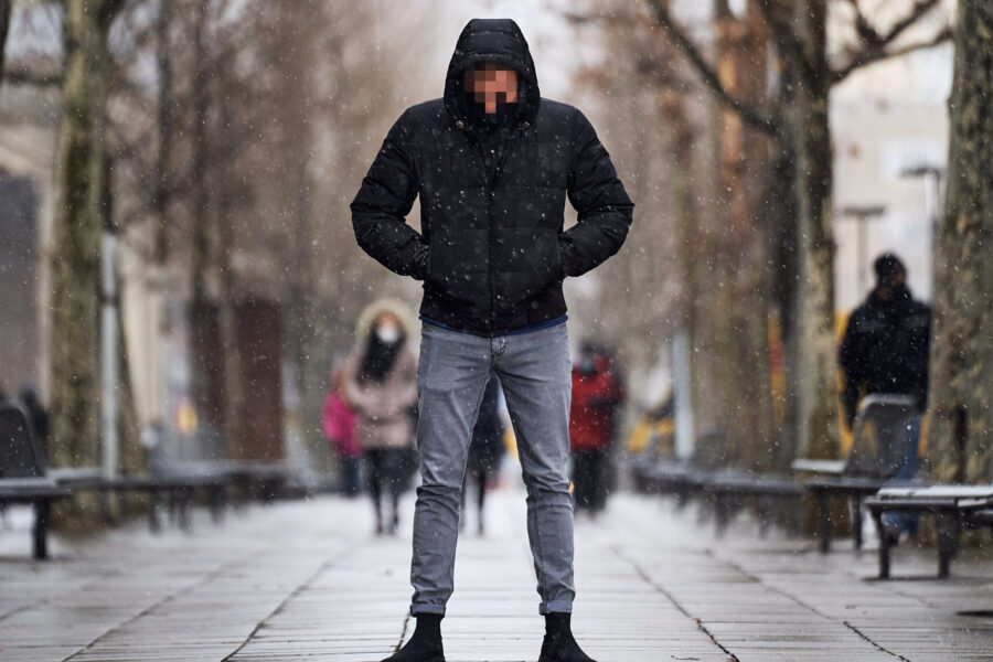 Person in schwarzer Jacke und Jeans geht in verschneiter Straße.