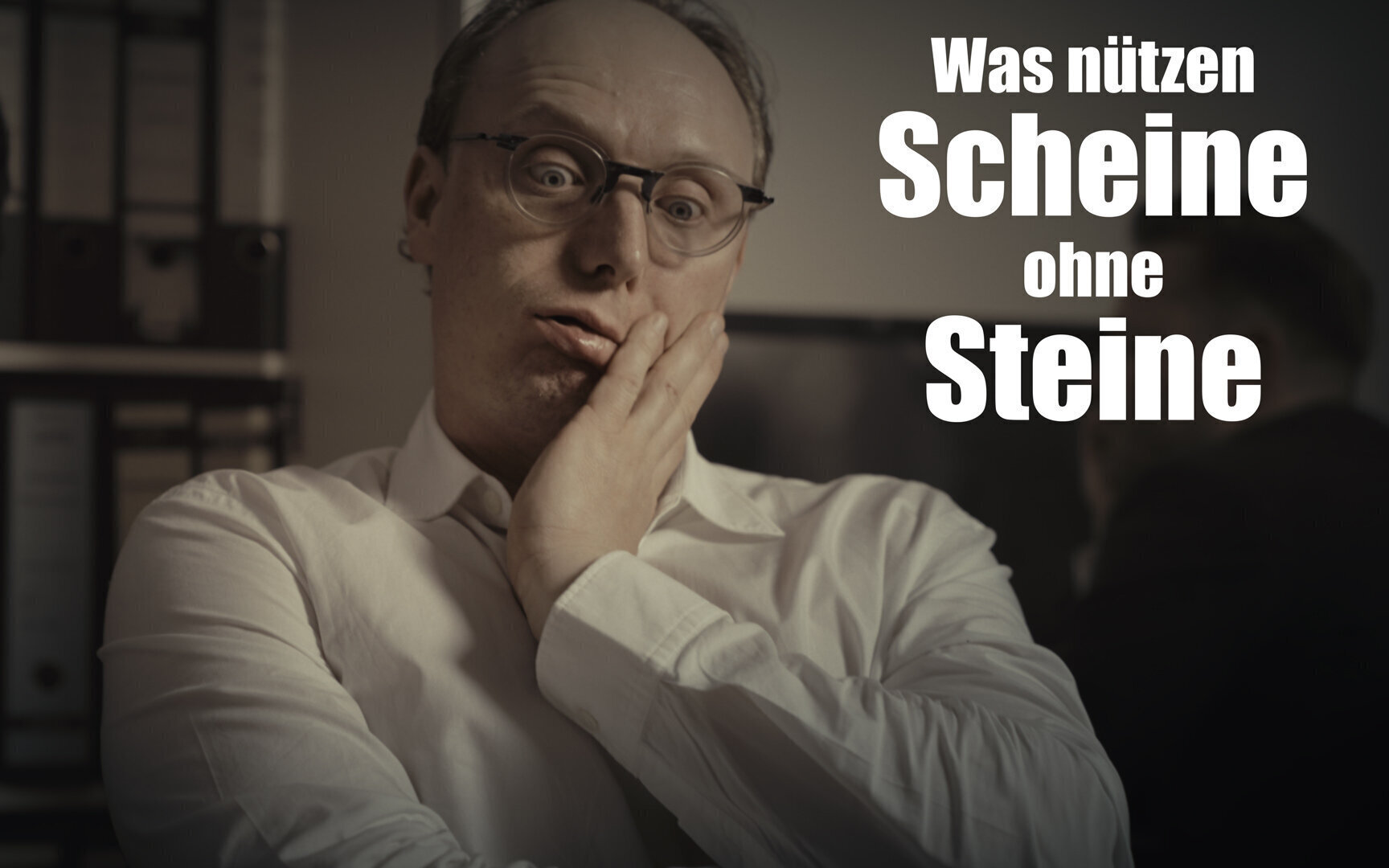 Mann im weißen Hemd, Hand am Gesicht, steht vor Aktenordnern. Text: „Was nützen Scheine...“