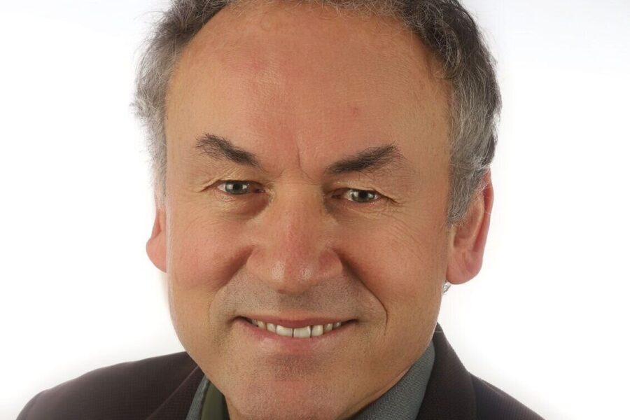 Ein lächelnder Mann in Hemd und Sakko vor weißem Hintergrund.