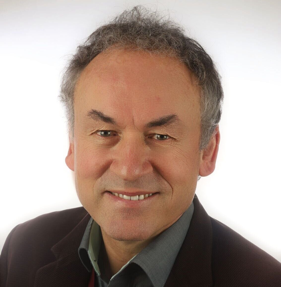 Ein lächelnder Mann in Hemd und Sakko vor weißem Hintergrund.