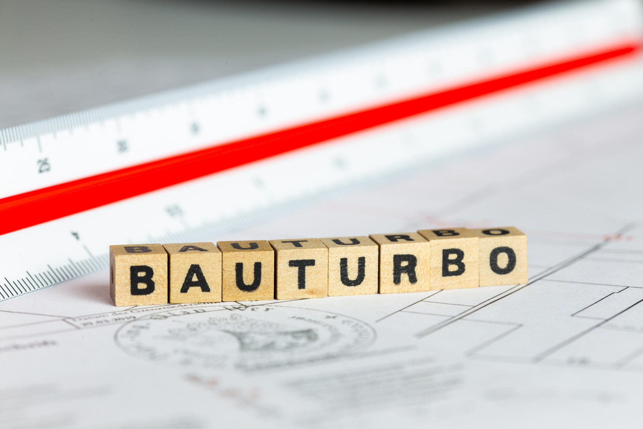 Holzklötze mit Buchstaben "BAUTURBO", daneben ein Lineal auf Plänen.