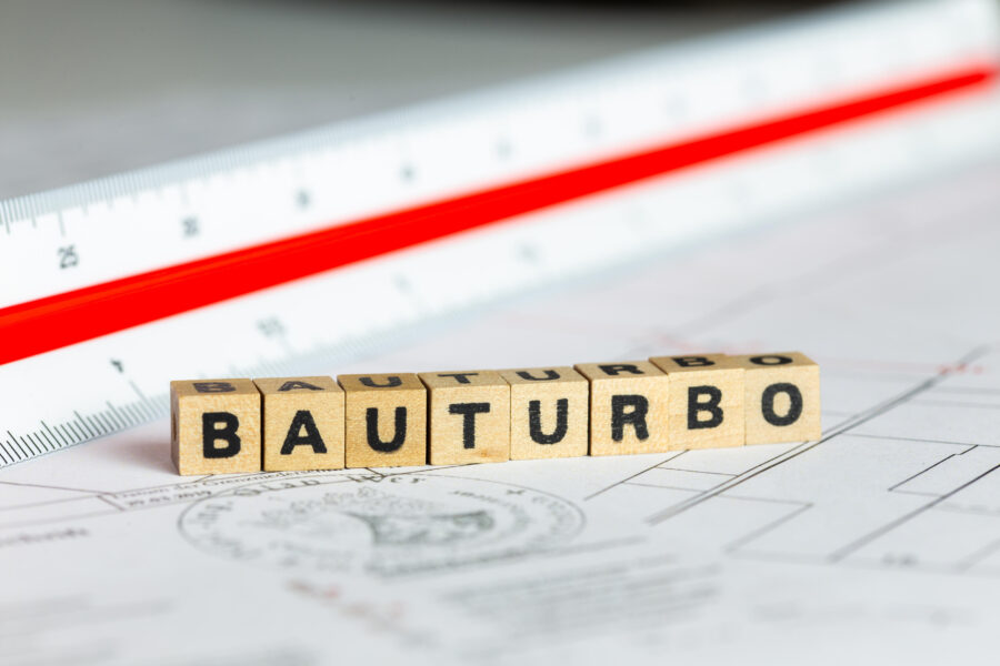 Holzklötze mit Buchstaben "BAUTURBO", daneben ein Lineal auf Plänen.