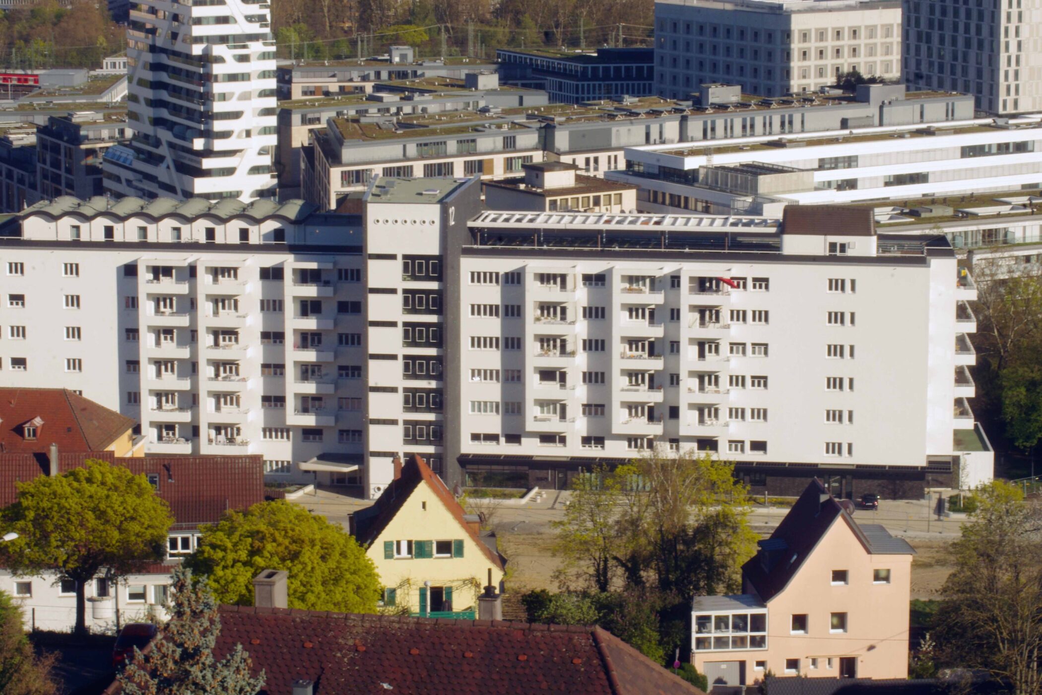 Verschiedene Gebäude, im Vordergrund Bäume und kleinere Häuser, modernes Hochhaus.