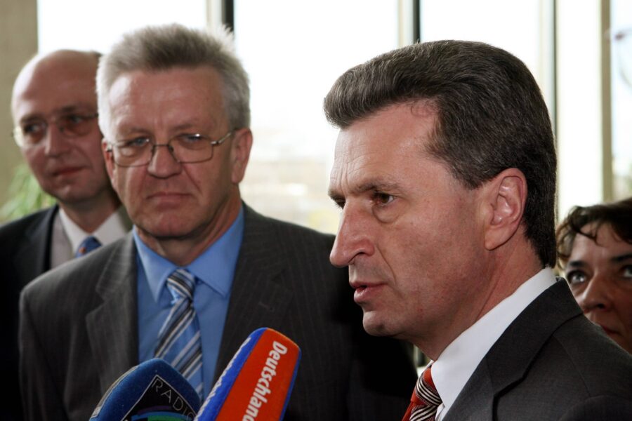 Vier Männer in Anzügen halten Mikrofone; einer spricht.