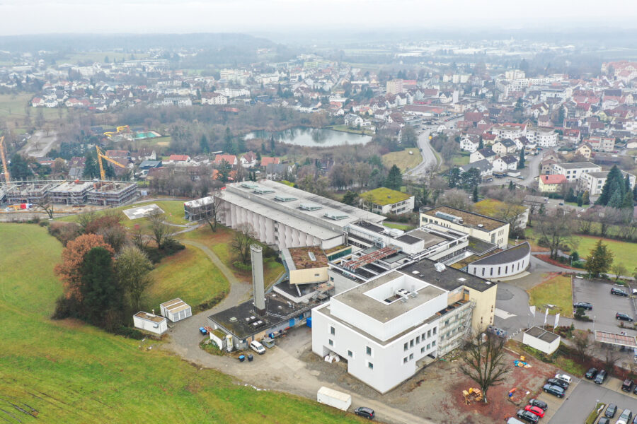 Großes Gebäude mit Flachdach, umgeben von Grünflächen und weiteren Gebäuden.