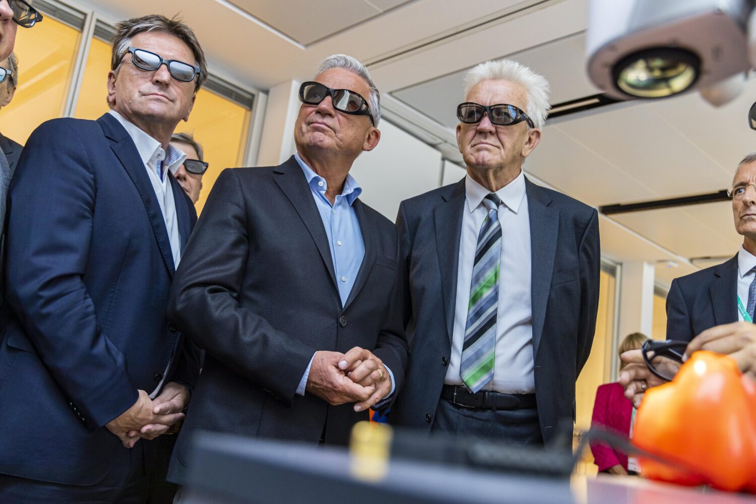 Fünf Personen in Anzügen und 3D-Brillen betrachten etwas.