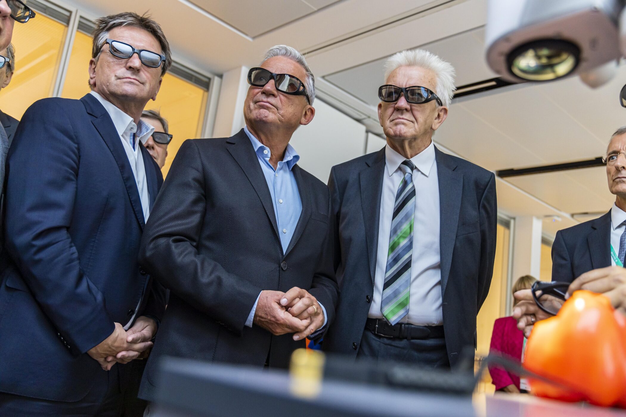 Fünf Personen in Anzügen und 3D-Brillen betrachten etwas.