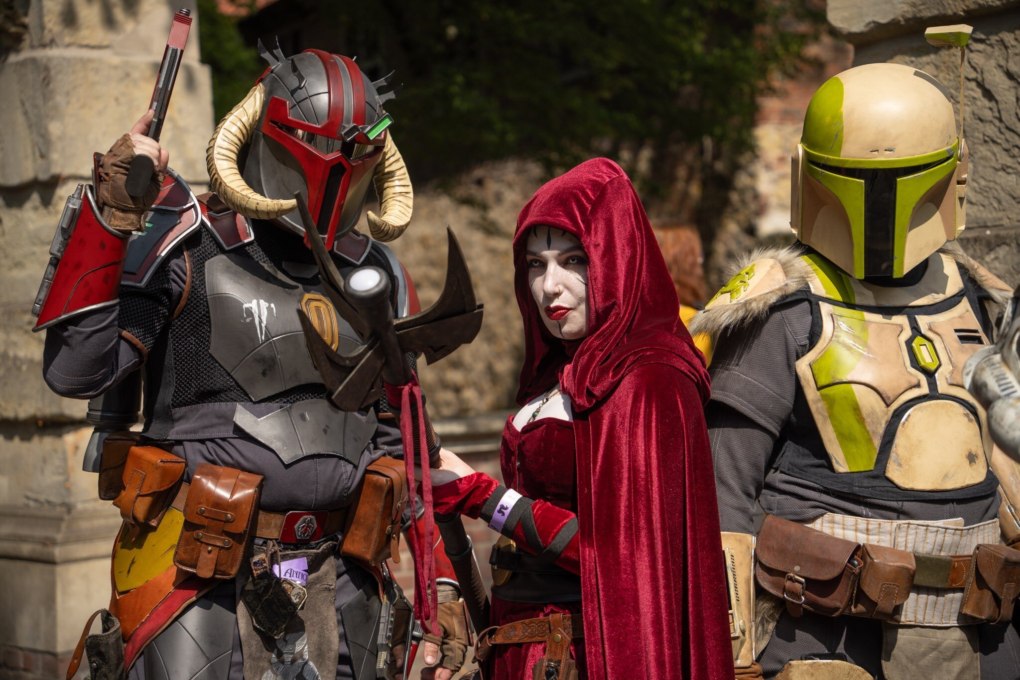 Drei Personen in futuristischen Kostümen, zwei mit Helmen, eine im roten Umhang.