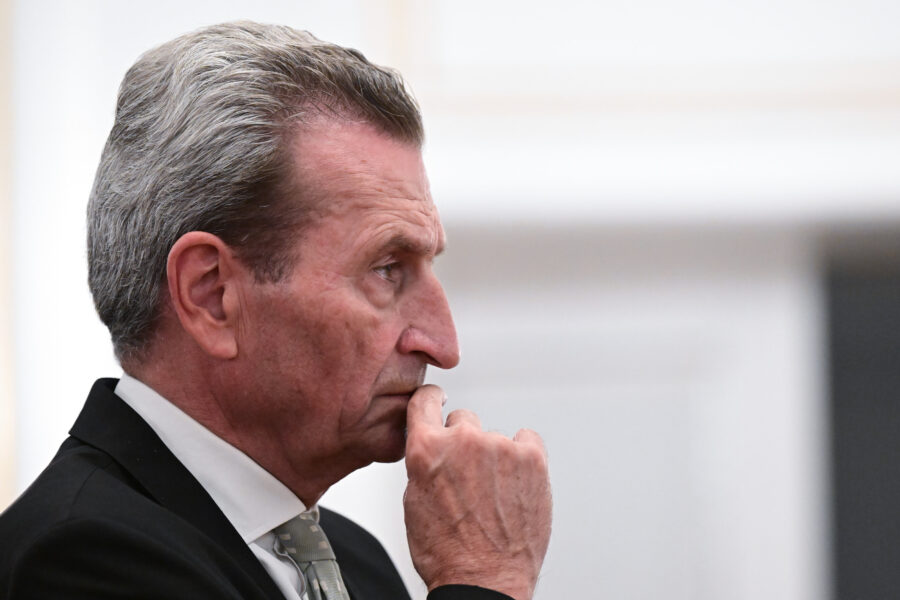 Älterer Mann in Anzug hält Hand an das Gesicht, profil vor hellem Hintergrund.