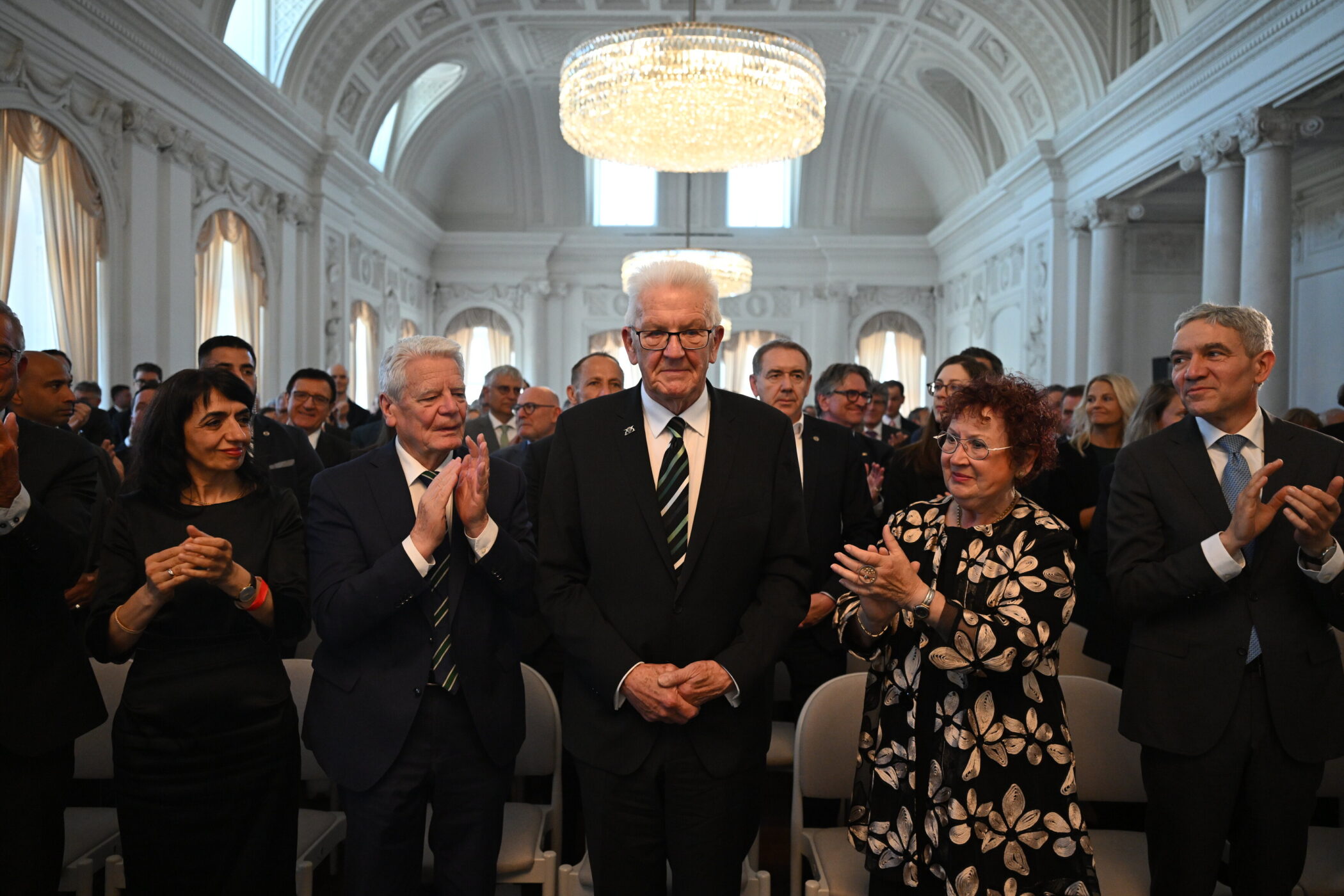Mehrere Personen in formeller Kleidung stehen in einem prunkvollen Saal.