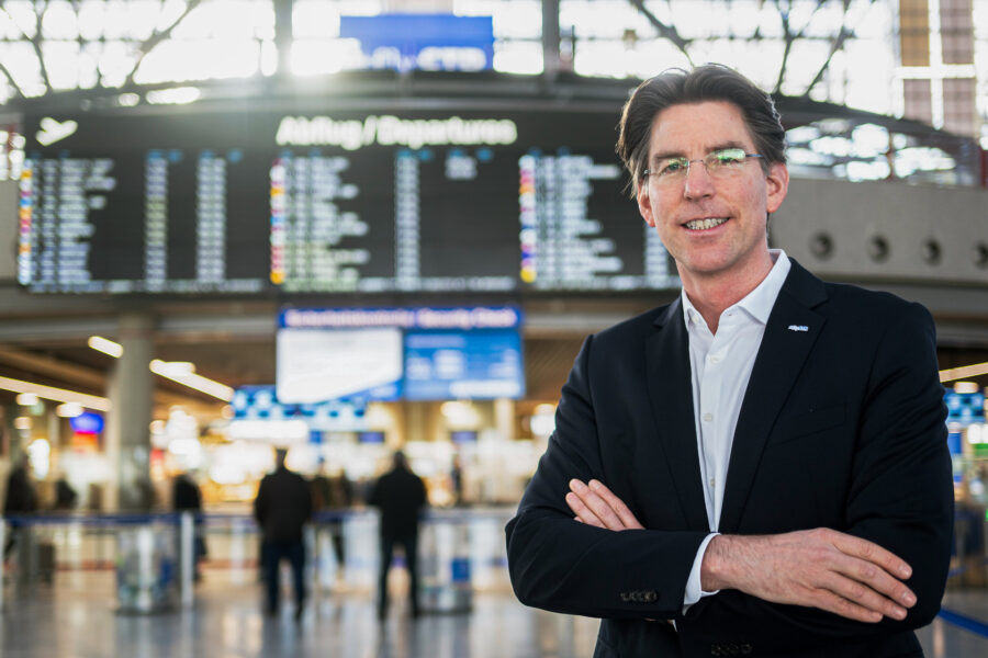 Eine Person in Anzug steht vor Anzeigetafel im Flughafen.