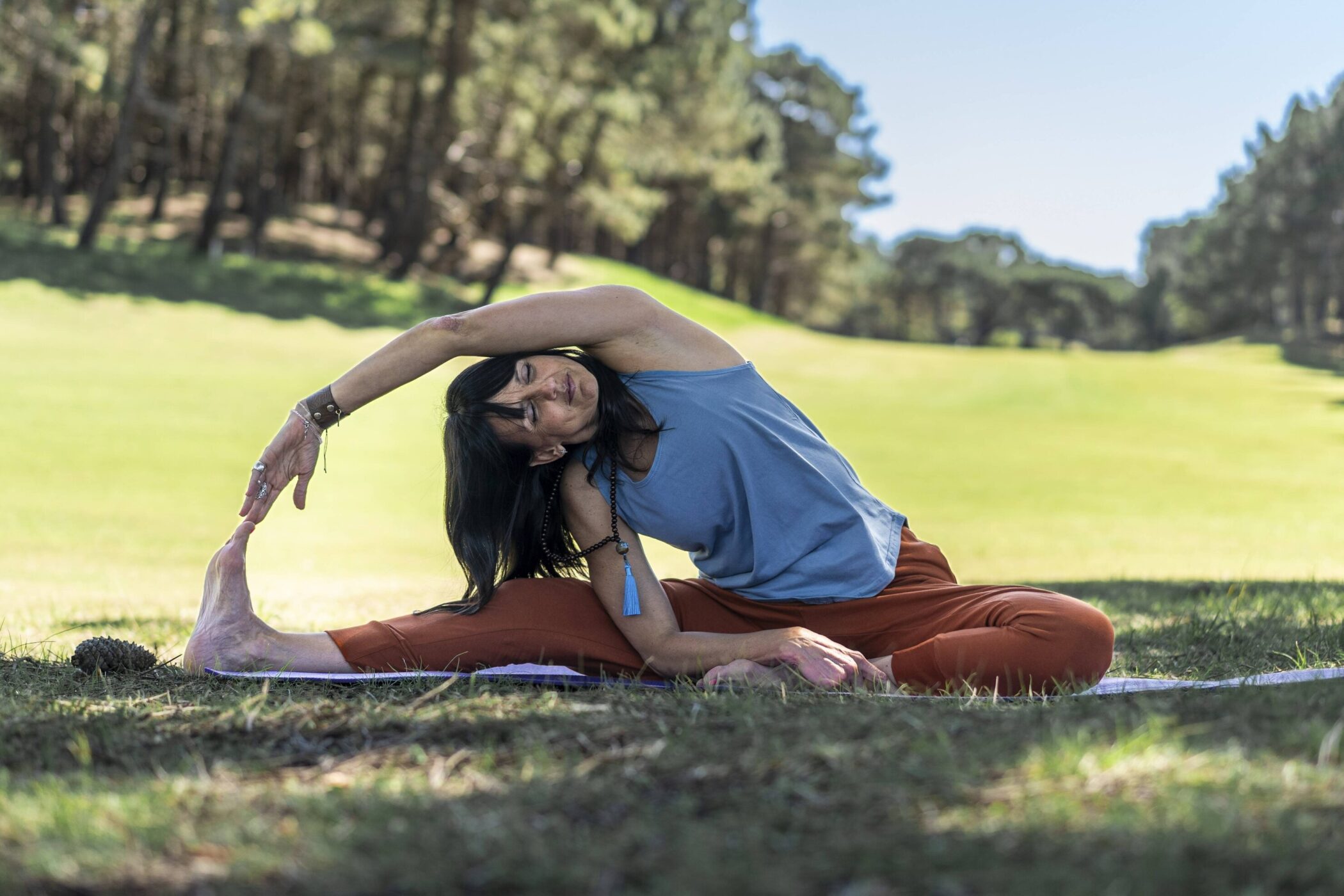 Person macht Yoga auf einer Wiese, Wald im Hintergrund.