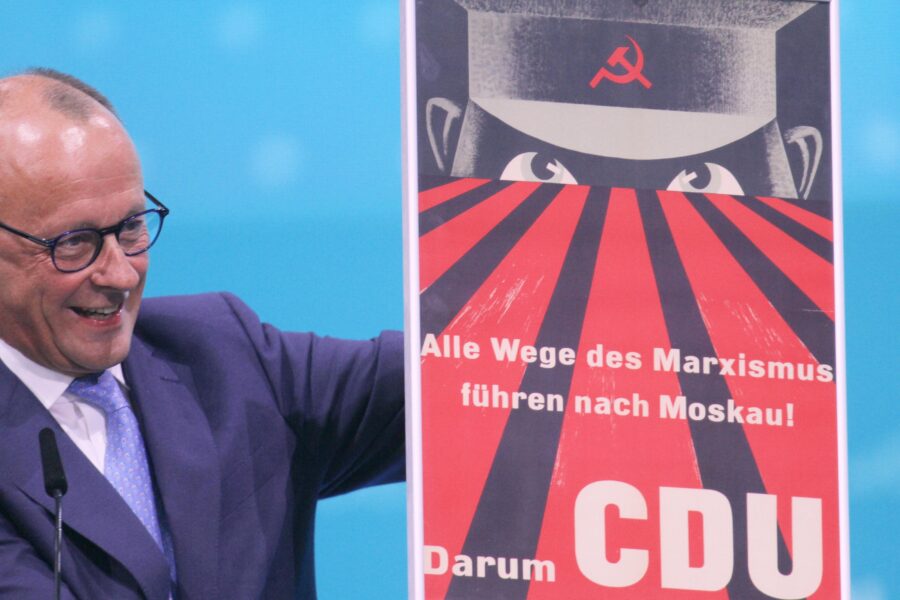 Mann hält Plakat mit kommunistischem Symbol und Text "Alle Wege des Marxismus führen... CDU".