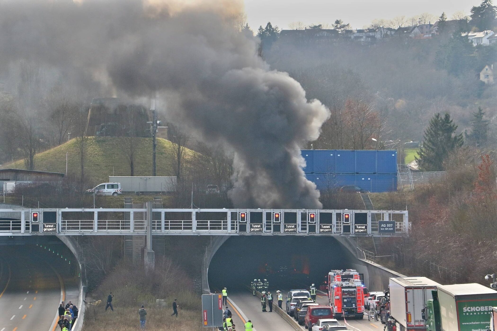 Dichter schwarzer Rauch über einem Straßentunnel, mehrere Einsatzfahrzeuge vor Ort.