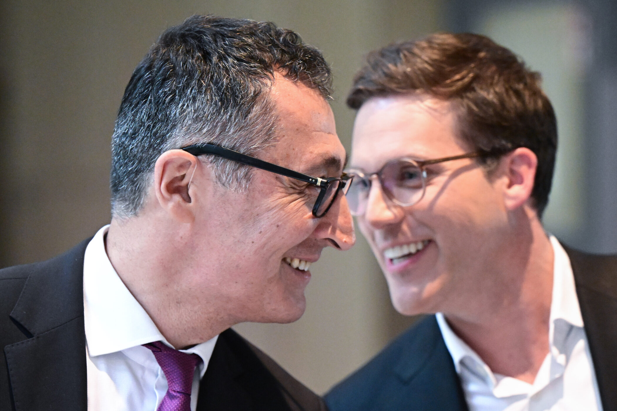 Zwei lächelnde Männer in Anzügen unterhalten sich nah beieinander.