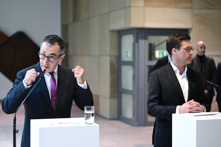 Zwei Männer im Anzug stehen an Rednerpulten und sprechen ins Mikrofon.