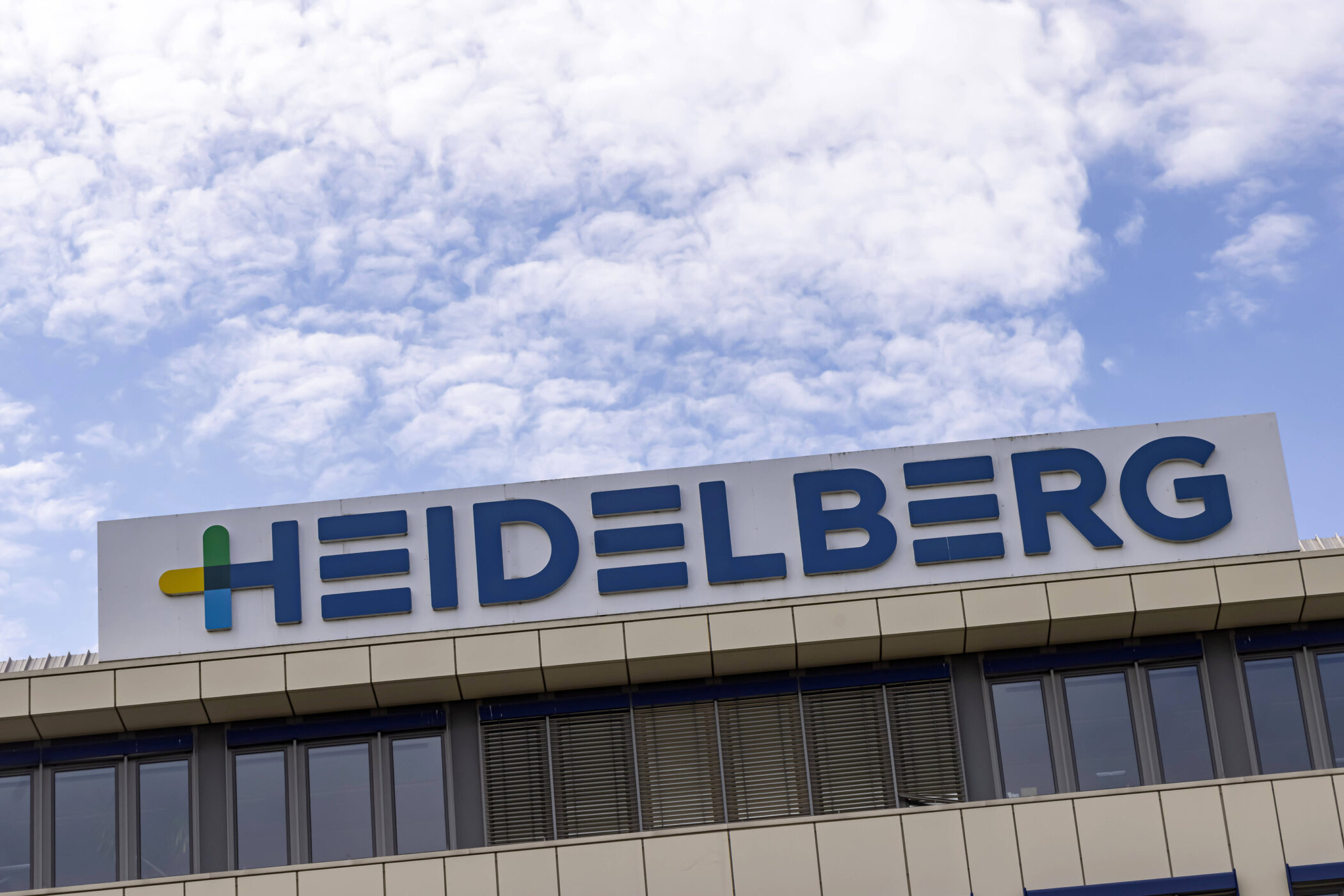 Gebäude mit "HEIDELBERG"-Schriftzug auf dem Dach vor bewölktem Himmel.