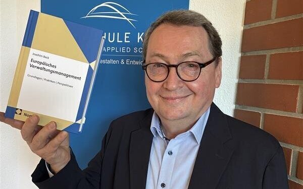 Mann hält ein Buch mit Titel "Europäisches Verwaltungsmanagement" vor blauem Schild.