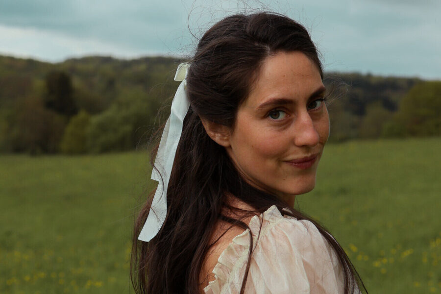 Frau blickt über die Schulter auf einer grünen Wiese mit bewölktem Himmel.