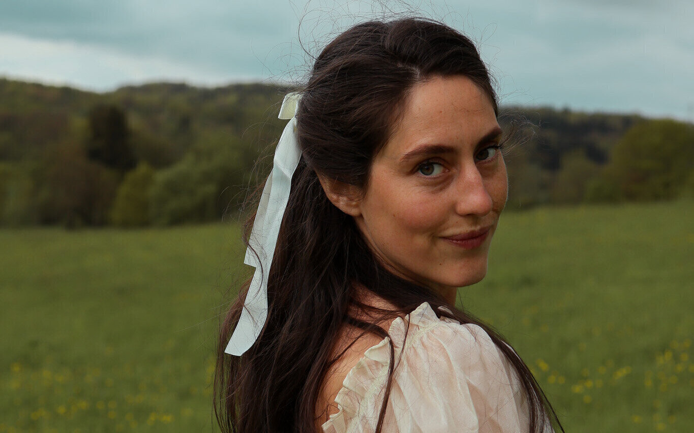 Frau blickt über die Schulter auf einer grünen Wiese mit bewölktem Himmel.