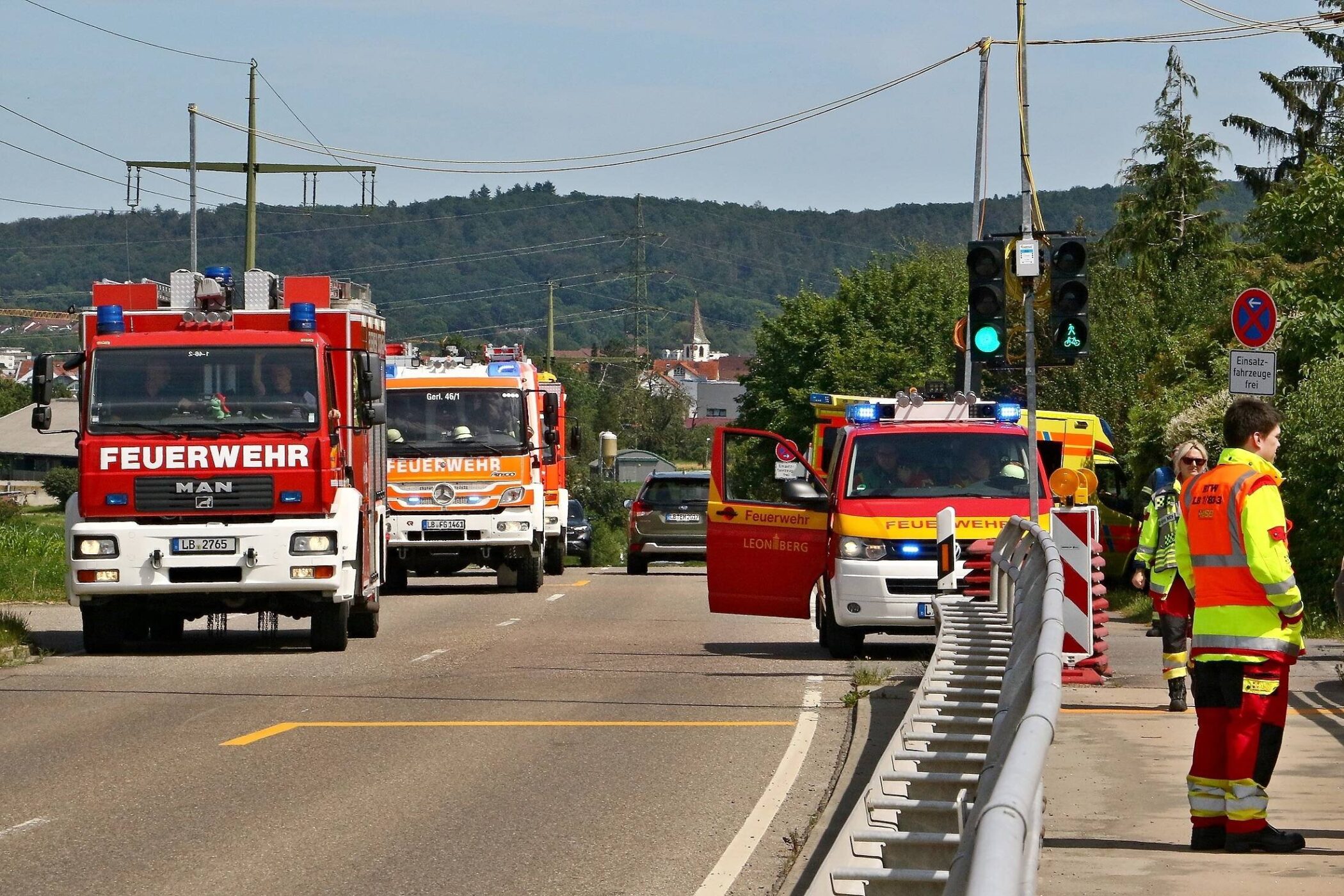 Feuerwehrautos auf Straße, Personen in Einsatzkleidung, grünes Ampellicht.