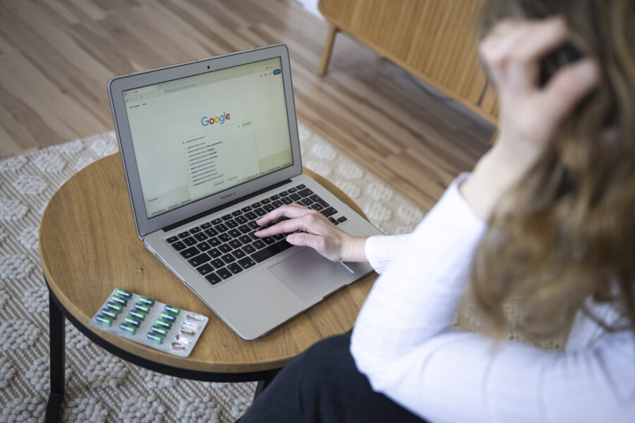 Person am Laptop, Tabletten auf einem Tisch daneben.