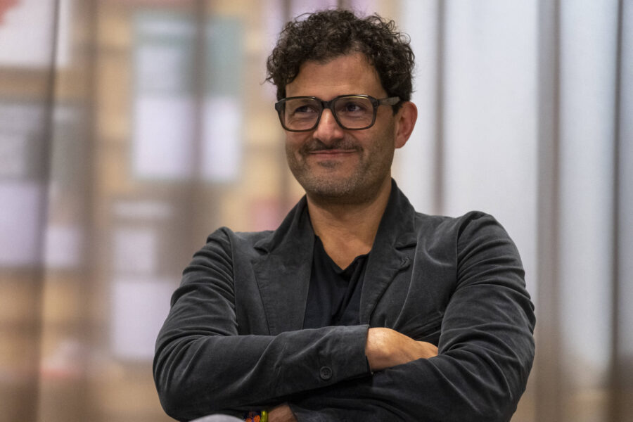 Person mit Brille und Bart, verschränkt die Arme, neutraler Hintergrund.