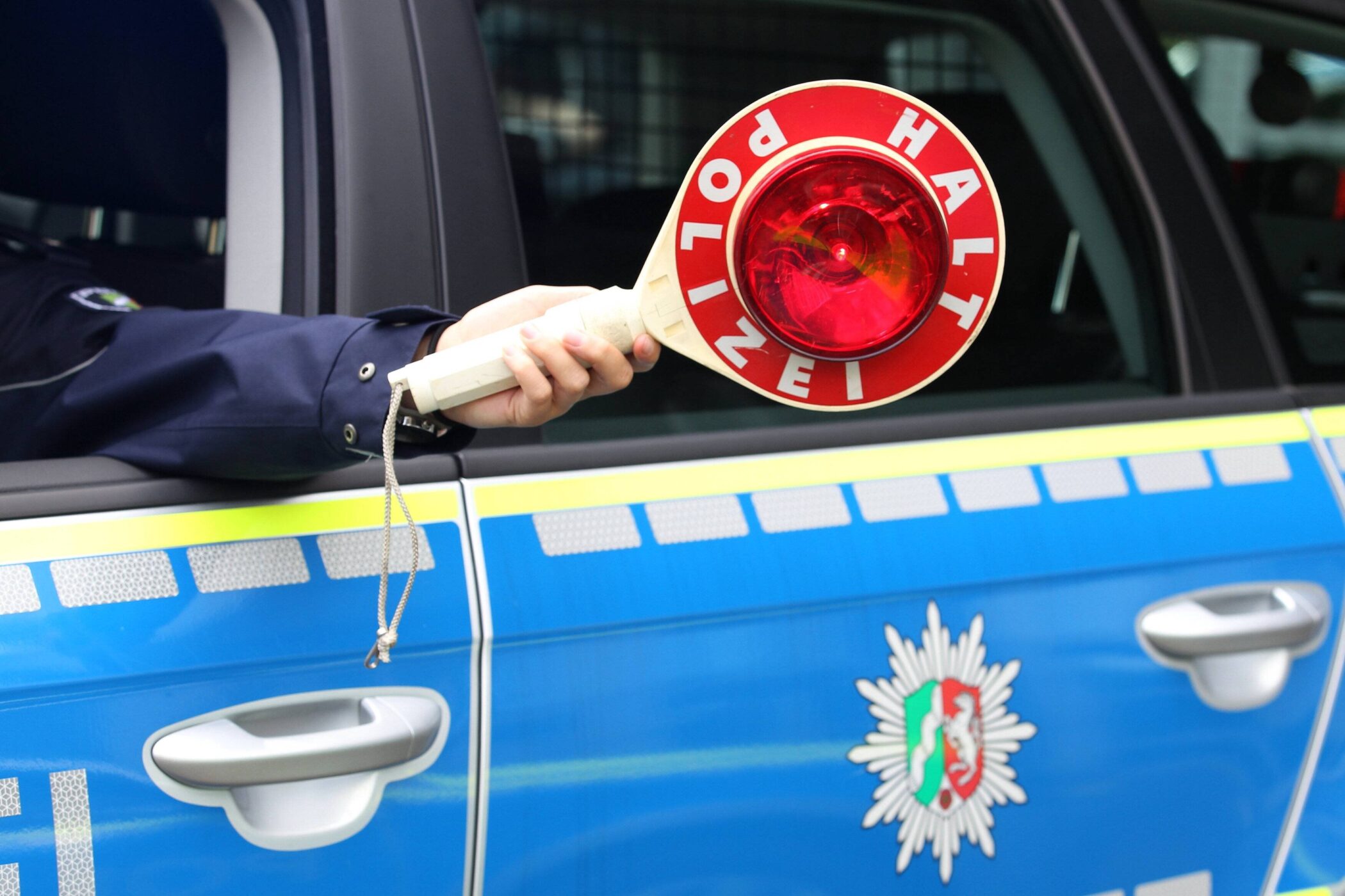 Eine Hand hält ein Polizeikelle mit "Halt Polizei" aus einem Autofenster.