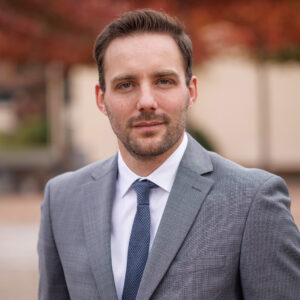 Ein Mann in Anzug mit Krawatte, unscharfer Hintergrund in herbstlichen Farben.