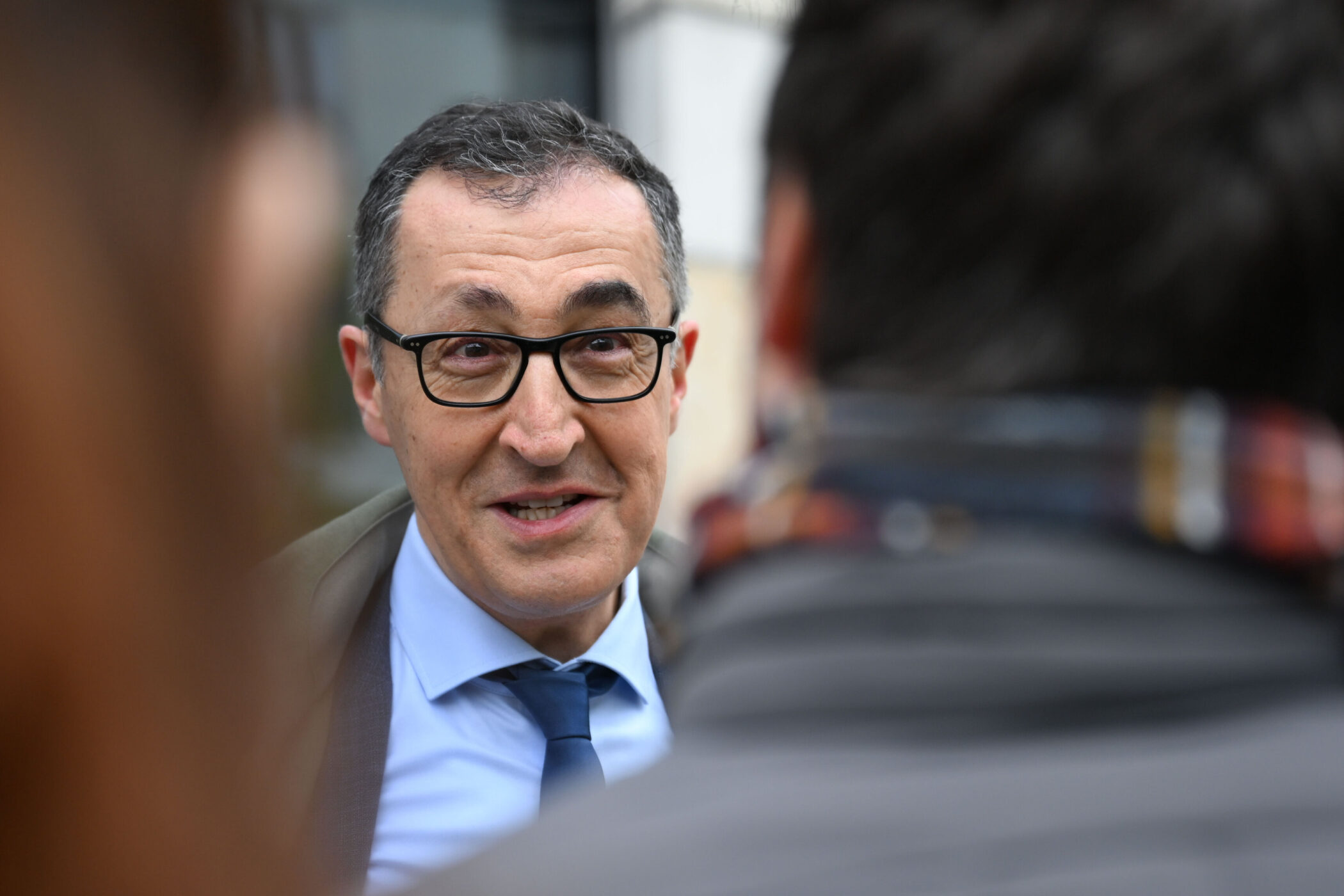 Mann mit Brille spricht, unscharfe Person im Vordergrund.