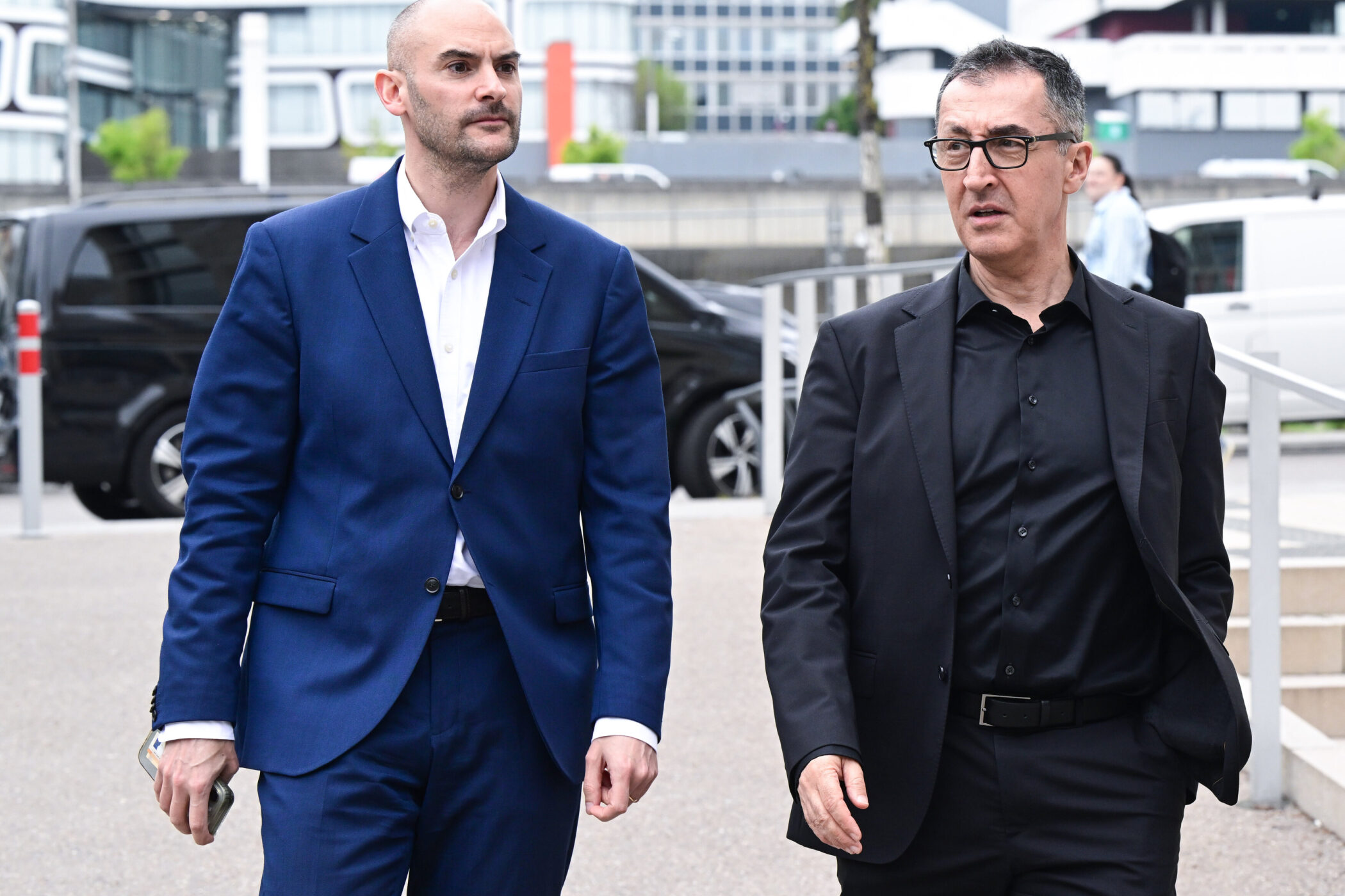 Zwei Männer in Anzügen gehen nebeneinander; Hintergrund moderne Gebäude.