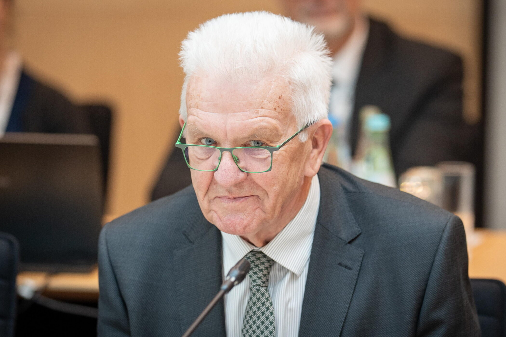 Älterer Mann mit Brille im Anzug bei einer Konferenz.